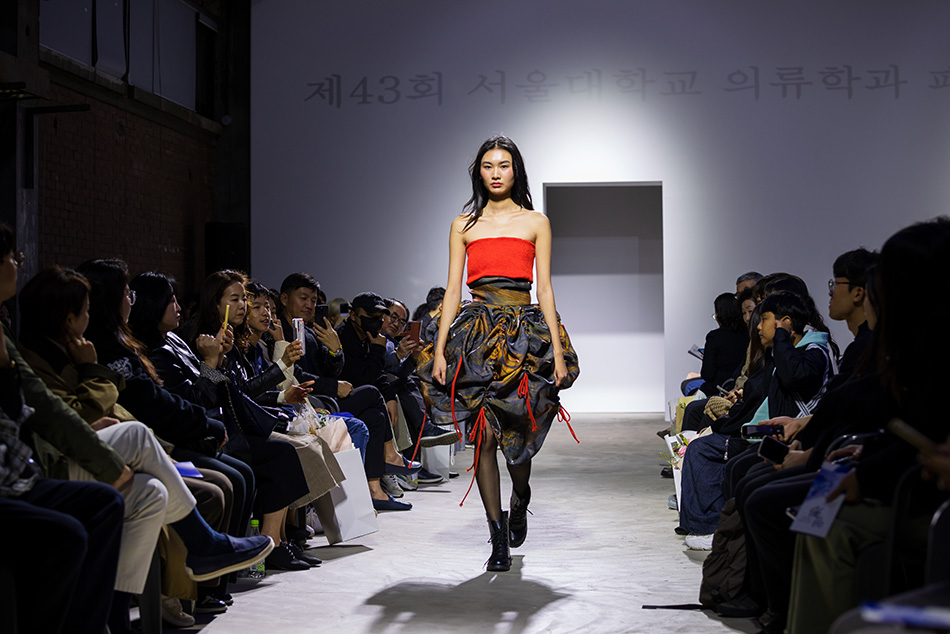 A model strides the runway, showcasing a unique, draped skirt.